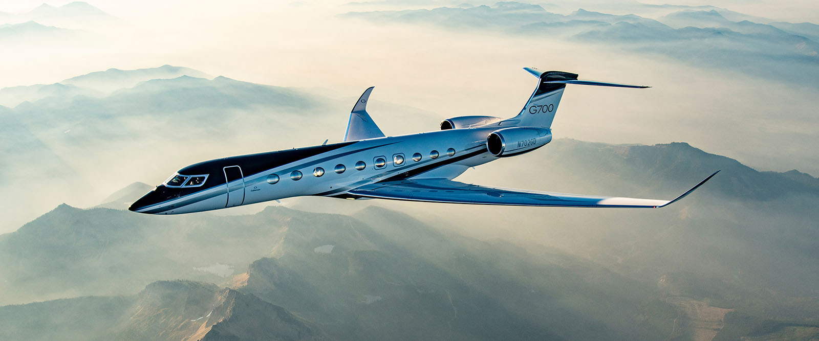 G700 flies over misty, sun-dappled mountain peaks