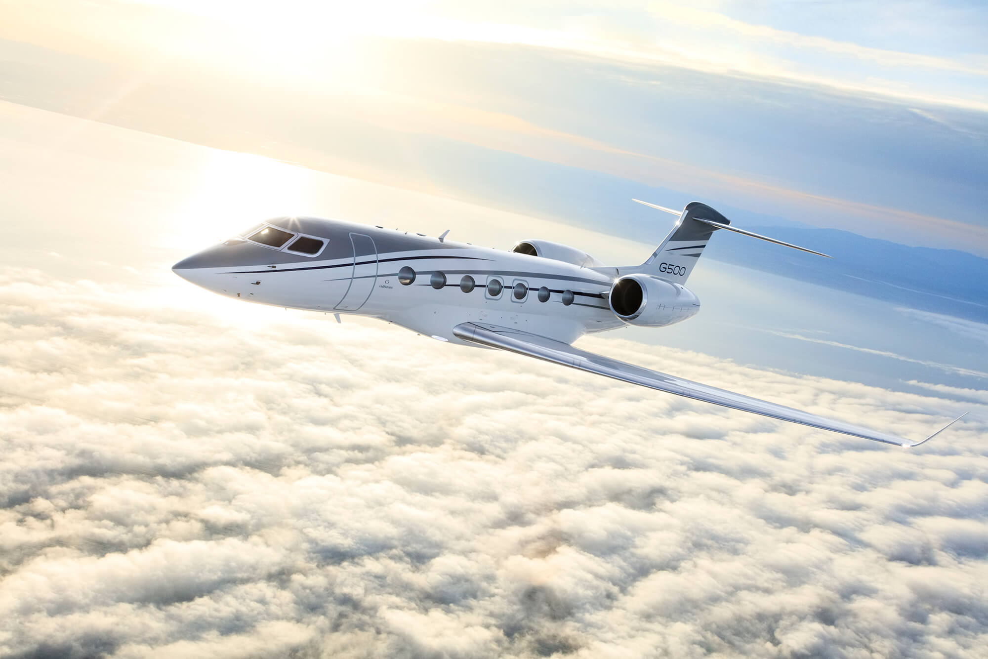 A Gulfstream G500 banks slightly over forested hills at twilight