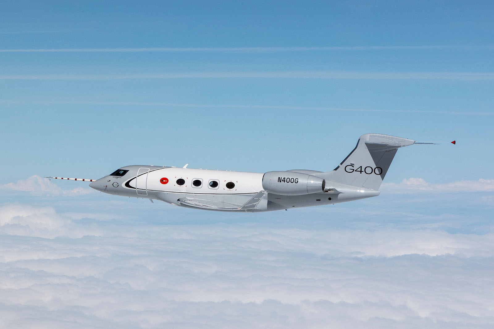 A G400 flies along a coastline and calm water toward the rising sun
