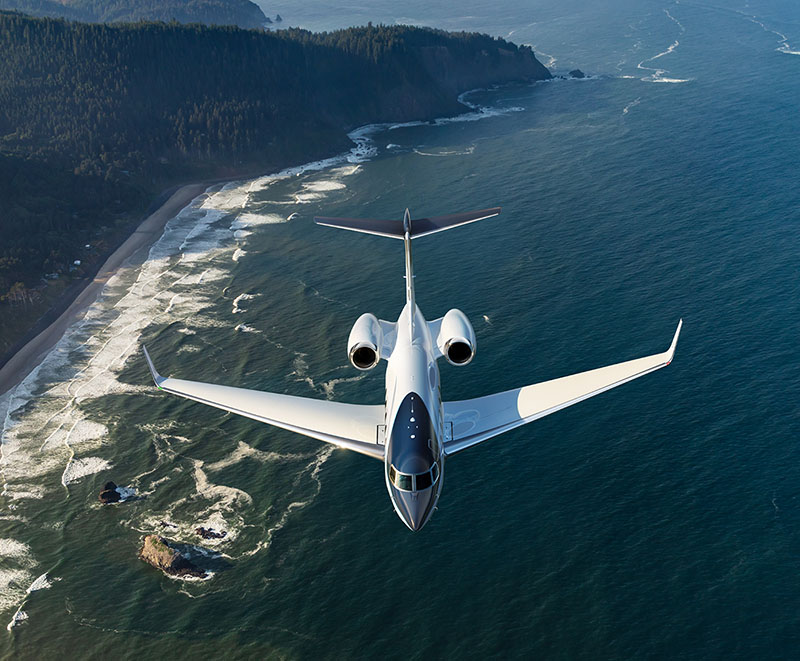G400 flying over a sunny, tree-covered coast
