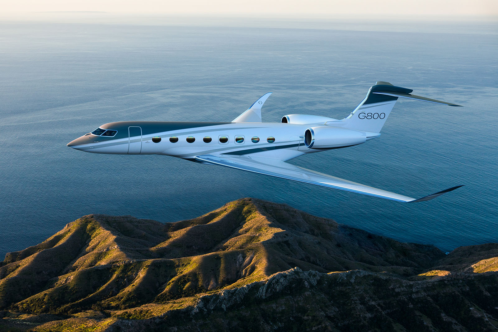 G800 climbing over a large body of water as it approaches a mountain range